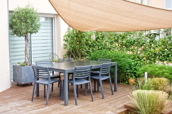 Graue Gartenmöbel auf einer Holzterrasse unter einem Sonnensegel.